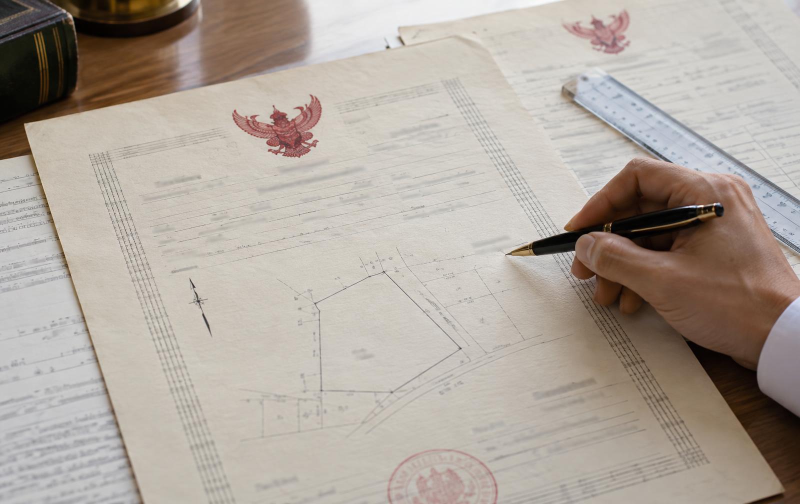 Thai land-title documents with red Garuda emblems being reviewed alongside a cadastral plan.